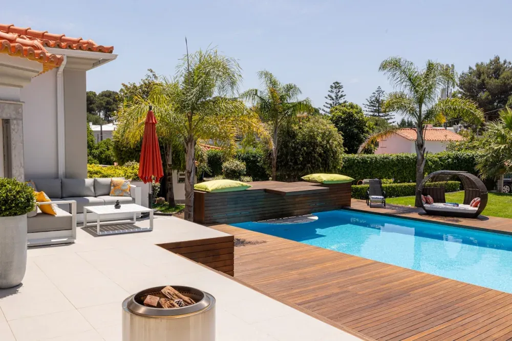 Modern pool deck with lounge furniture, fire bowl, and lush landscaping