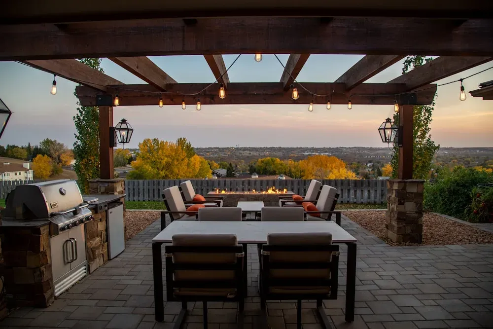 Covered pergola with dining area, built-in grill, and fire pit at golden hour